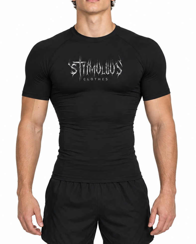 A man modeling a black short-sleeve athletic rash guard with a white stylized 'STIMULUS CLOTHES' logo on the chest, paired with black shorts, against a plain white background.