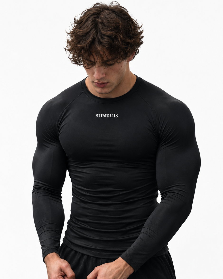 A muscular man wearing a tight-fitting black long-sleeve athletic shirt with 'STIMULIS' printed in white on the chest, paired with black shorts, against a plain white background.