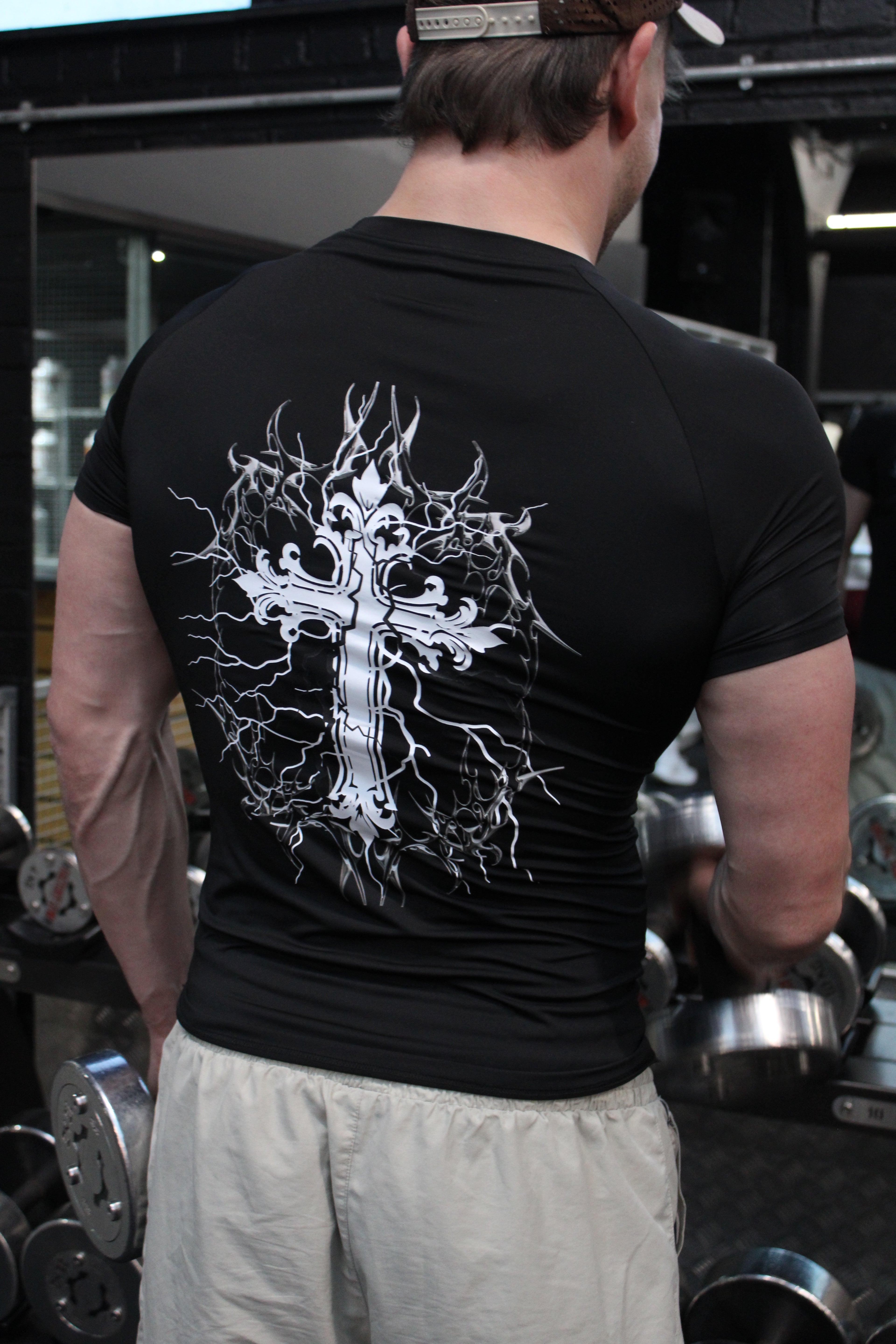 Person lifting weights with a black t-shirt featuring a white cross design.