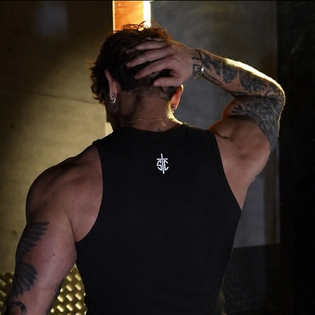 Person wearing a black SC tank top with visible tattoos in a dimly lit setting