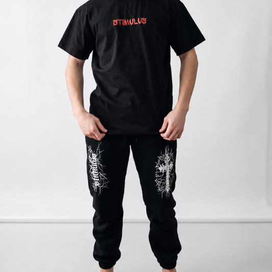 Person wearing a black t-shirt with red text and black pants with white patterns on a white background