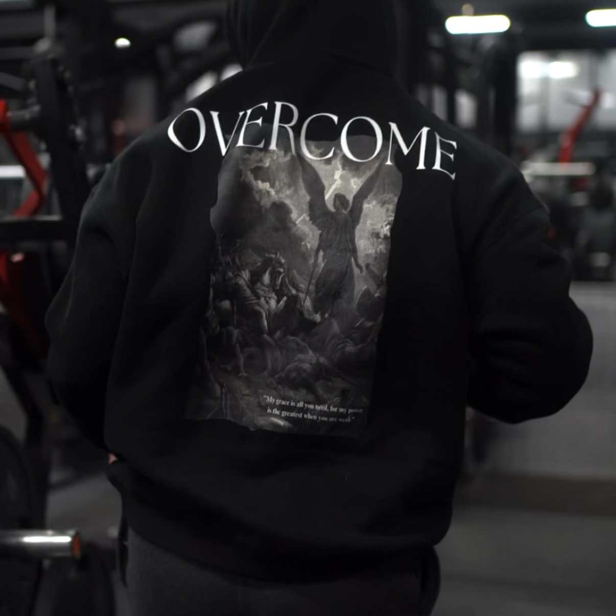 Person wearing a black hoodie with 'OVERCOME' printed on the back in a gym setting