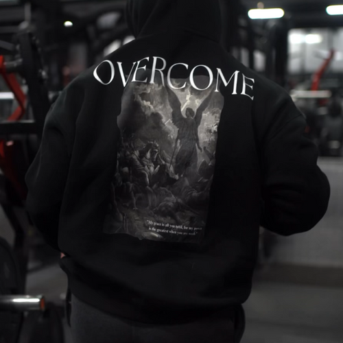 Person wearing a black hoodie with 'OVERCOME' printed on the back in a gym setting