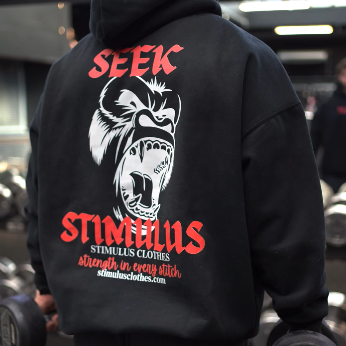 Person wearing a black hoodie with a graphic design and text in a gym setting