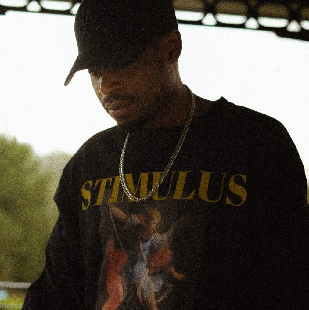 Person wearing a black hoodie with 'STIMULUS' text and a graphic design, standing outdoors.