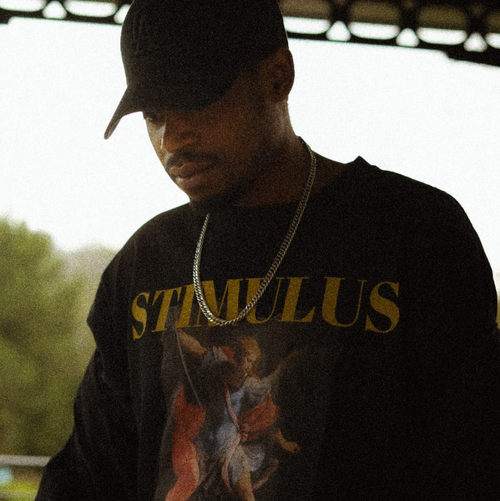 Person wearing a black hoodie with 'STIMULUS' text and a graphic design, standing outdoors.