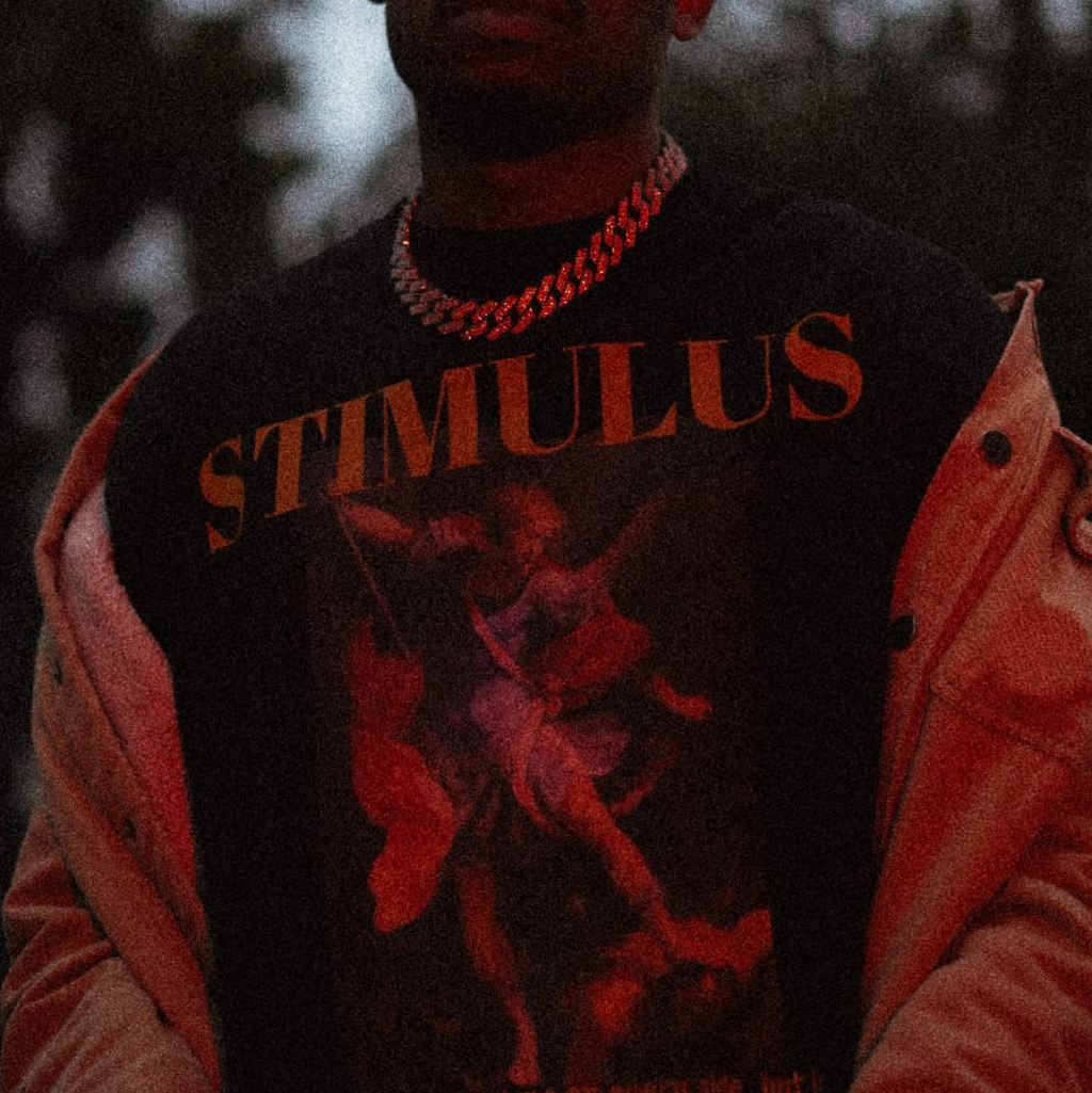 Person wearing a 'Stimulus' shirt with a graphic design, standing against a dark background.