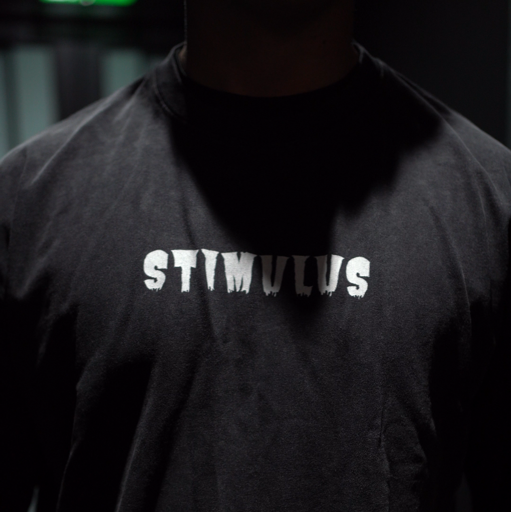 Person wearing a black shirt with 'STIMULUS' text in a dark setting