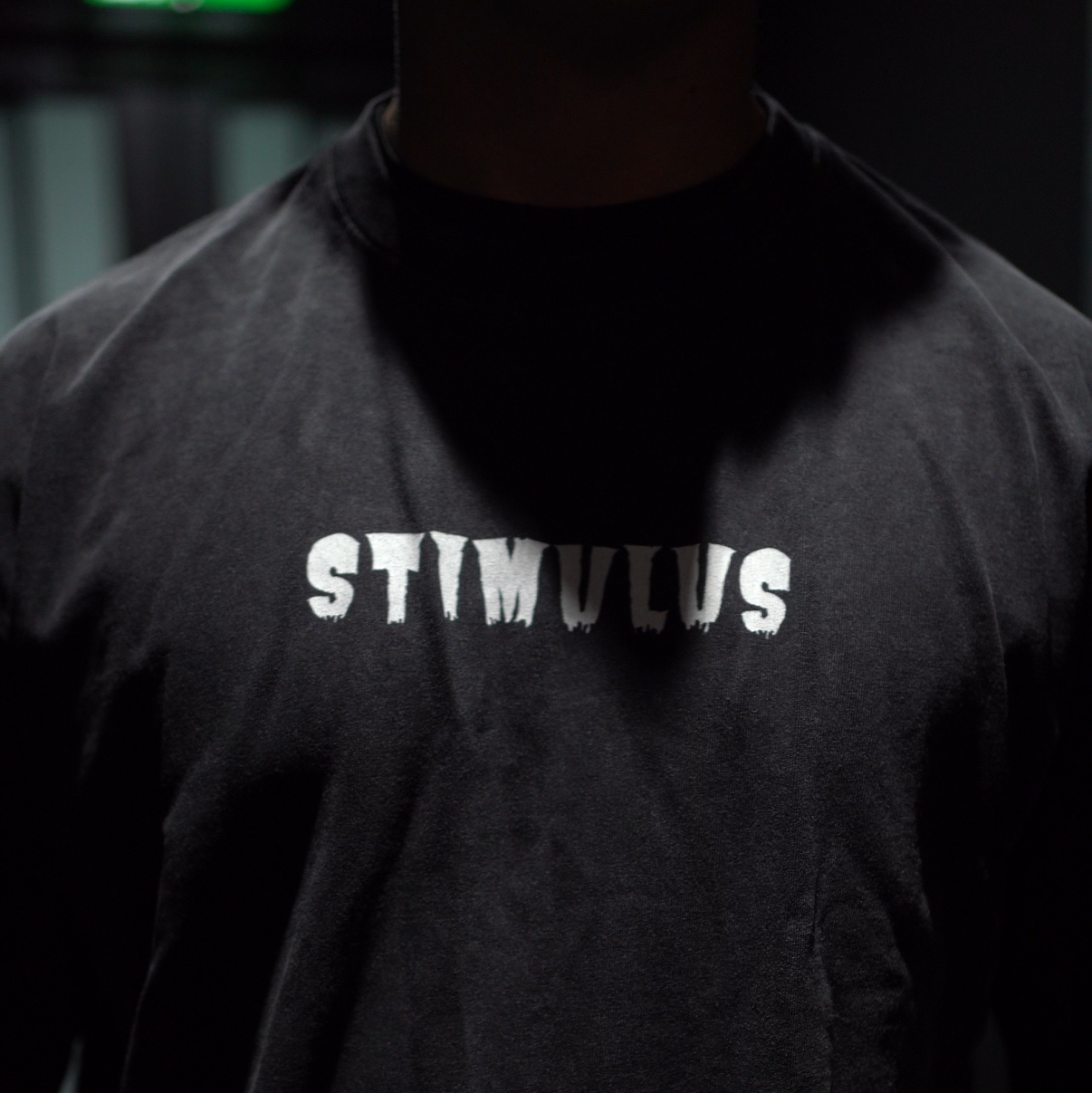 Person wearing a black shirt with 'STIMULUS' text in a dark setting
