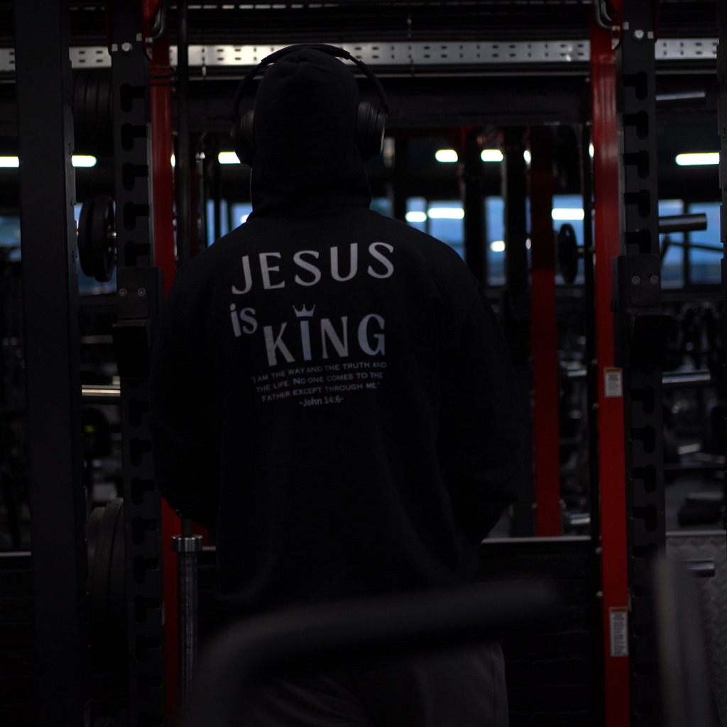 Person wearing a hoodie with 'Jesus is King' text in a dark setting