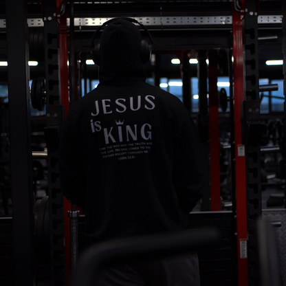 Person wearing a hoodie with 'Jesus is King' text in a dark setting