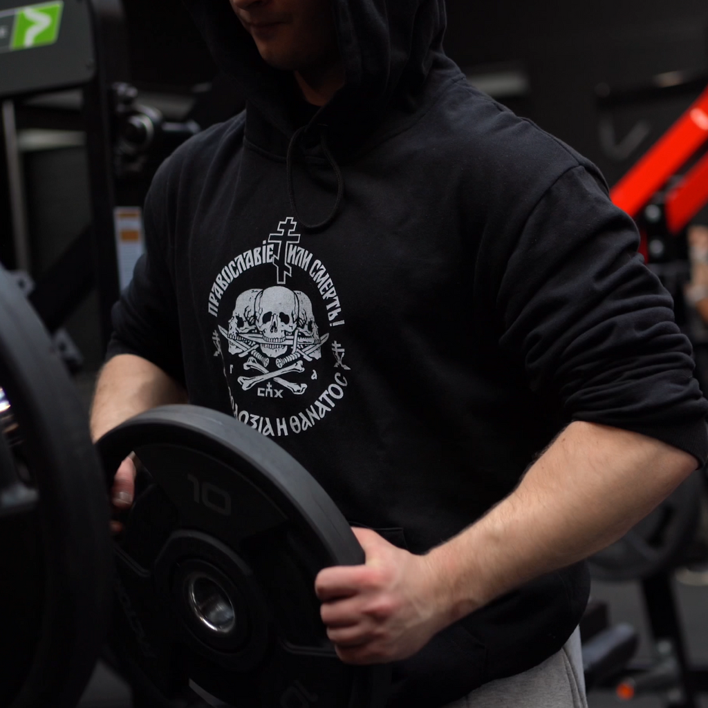 Person wearing a black hoodie with a logo in a gym setting