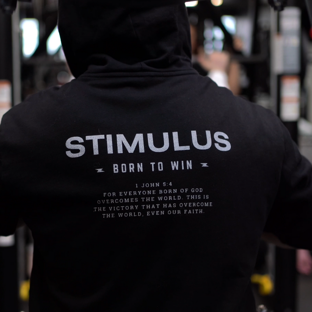 Person wearing a black hoodie with 'STIMULUS' branding in a dark setting