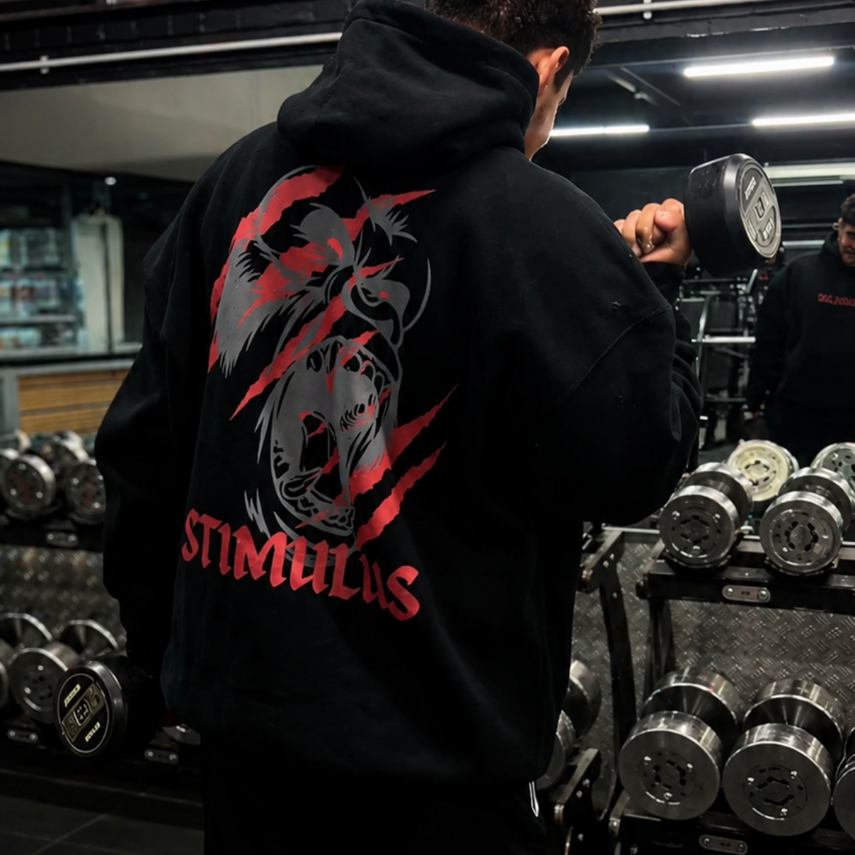 Person wearing a black hoodie with a red and white logo in a gym setting