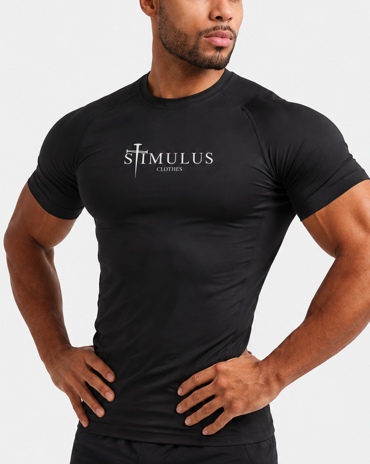A muscular man wearing a black tight-fitting short-sleeve athletic compression shirt with 'STIMULUS' printed on the chest, paired with matching black athletic shorts, against a light gray studio background.